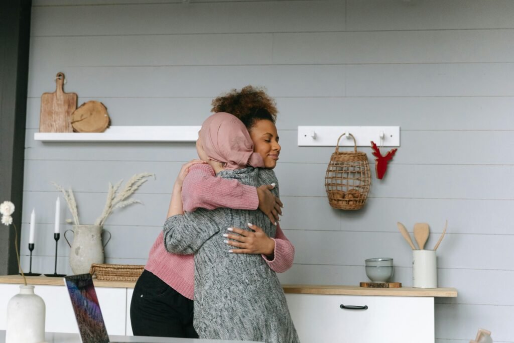 Two women share a heartfelt hug in a cozy kitchen, symbolizing support and connection.